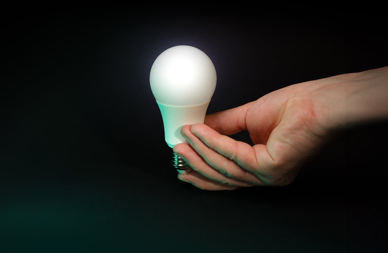 A hand holding an illuminated LED bulb against a dark background.